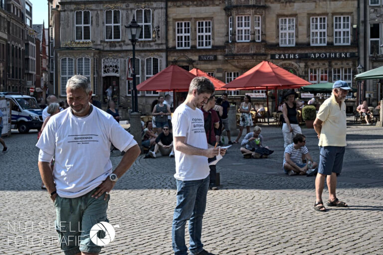 Mitglieder der Gruppe mit bedruckten Shirts, die für” Querdenken 421 Bremen” auf dem Marktplatz werben.