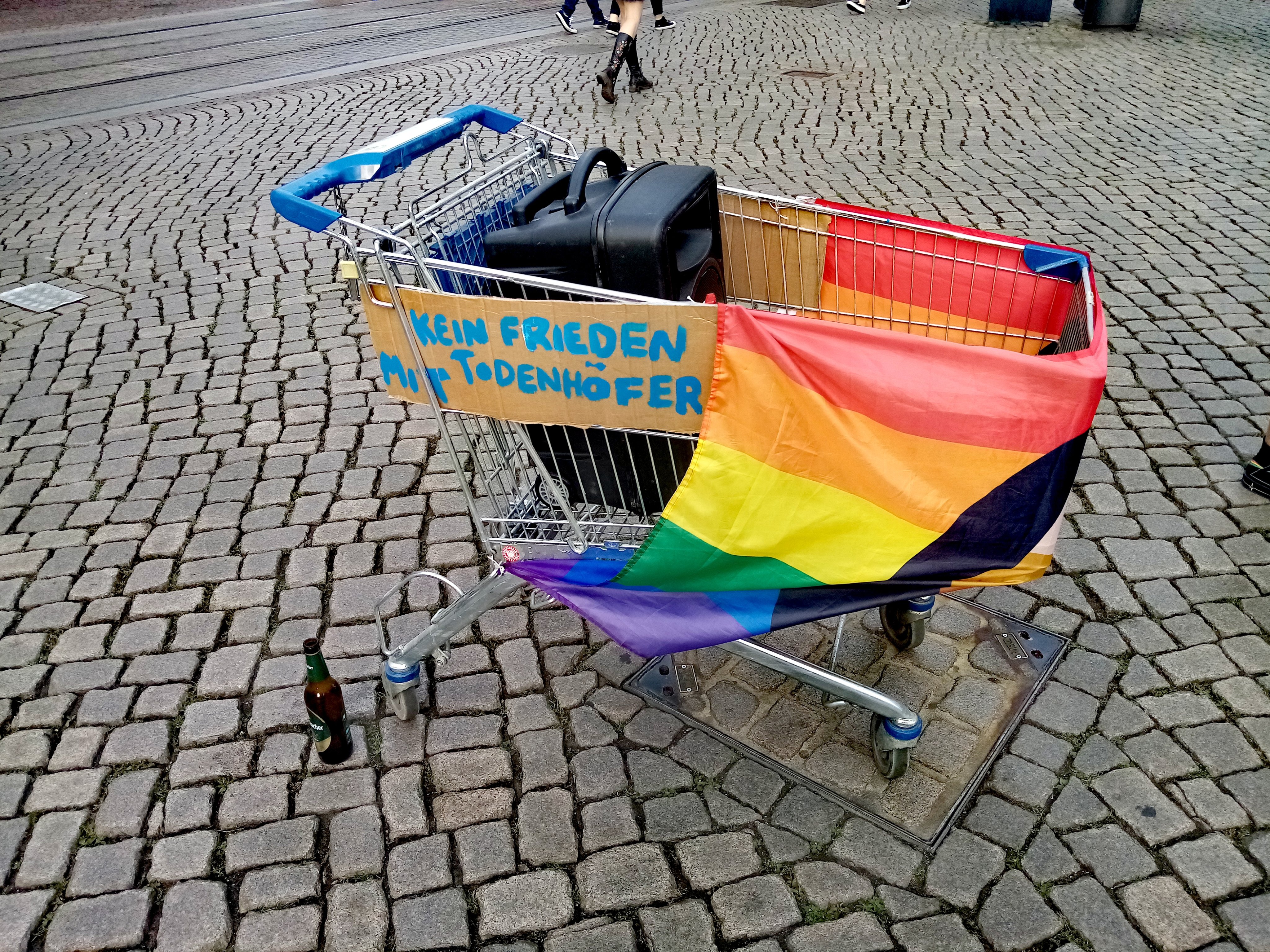 Ein Einkaufswagen mit Lautsprecher, Regenbogenflagge und dem Schild Kein Frieden mit Todenhöfer.