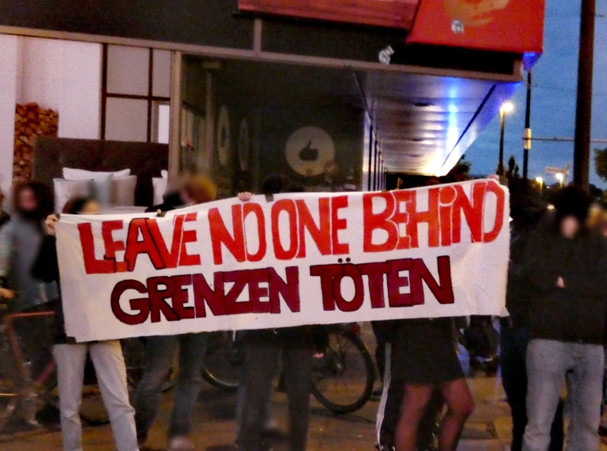 Demonstrierende halten ein Transparent mit den Aufschriften „Leave no one behind“ und „Grenzen töten“.