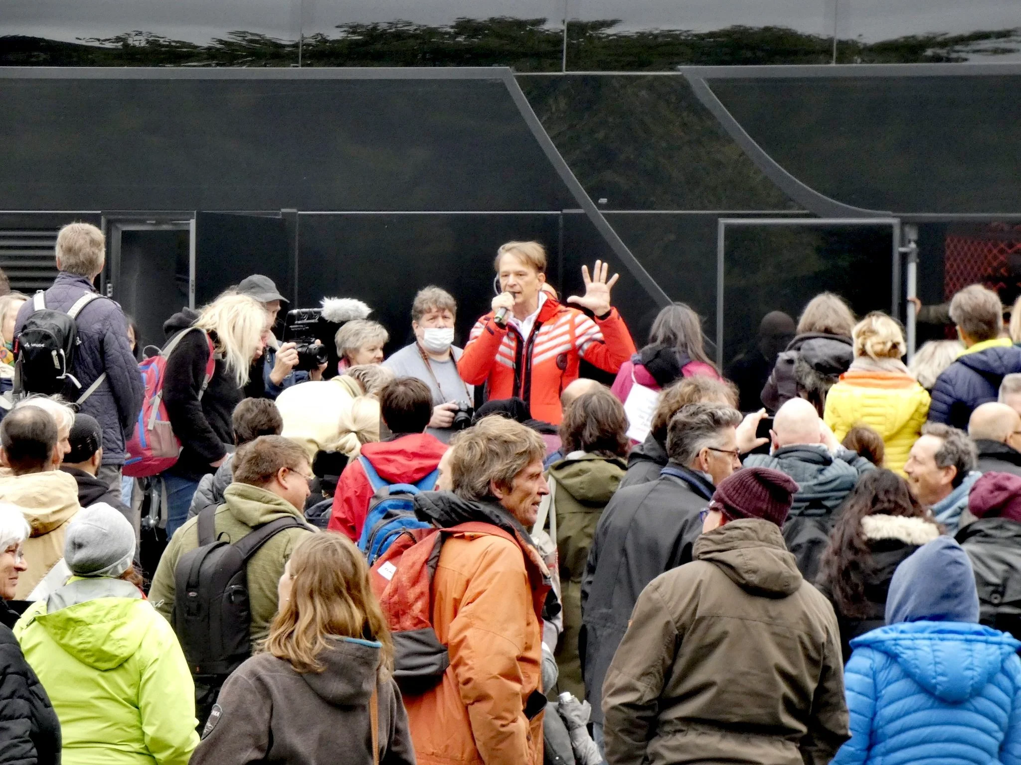 Bodo Schiffmann spricht mit einem Mikrofon vor einem schwarzen Reisebus; zahlreiche Menschen stehen vor ihm.