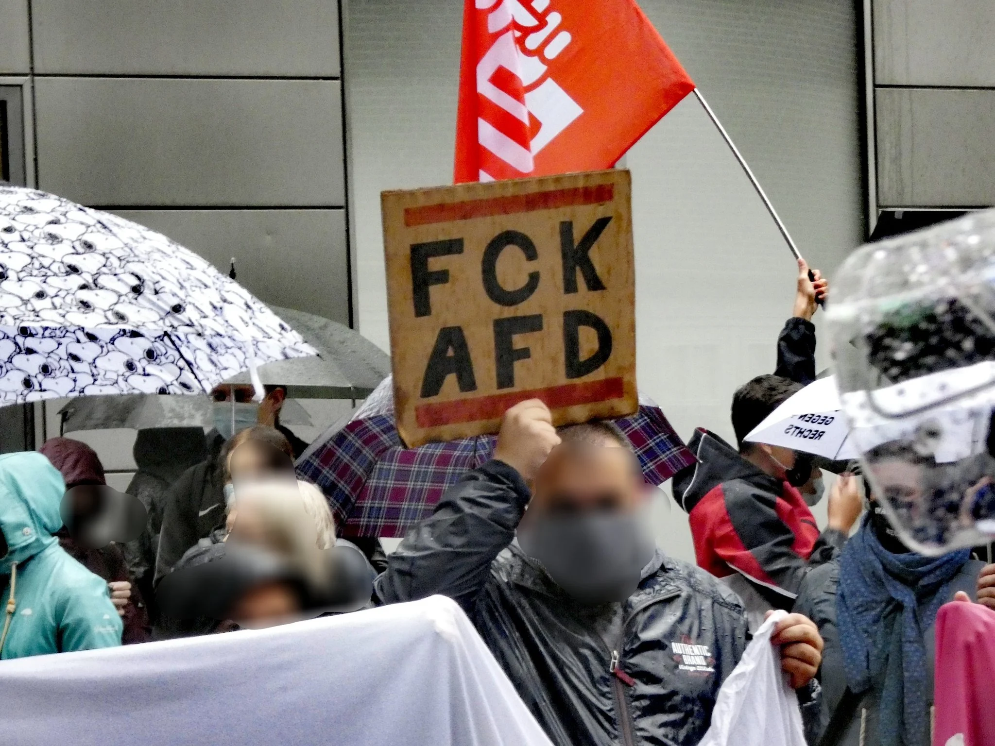 Demonstrierende unter Regenschirmen halten ein Schild mit der Aufschrift „FCK AFD“.