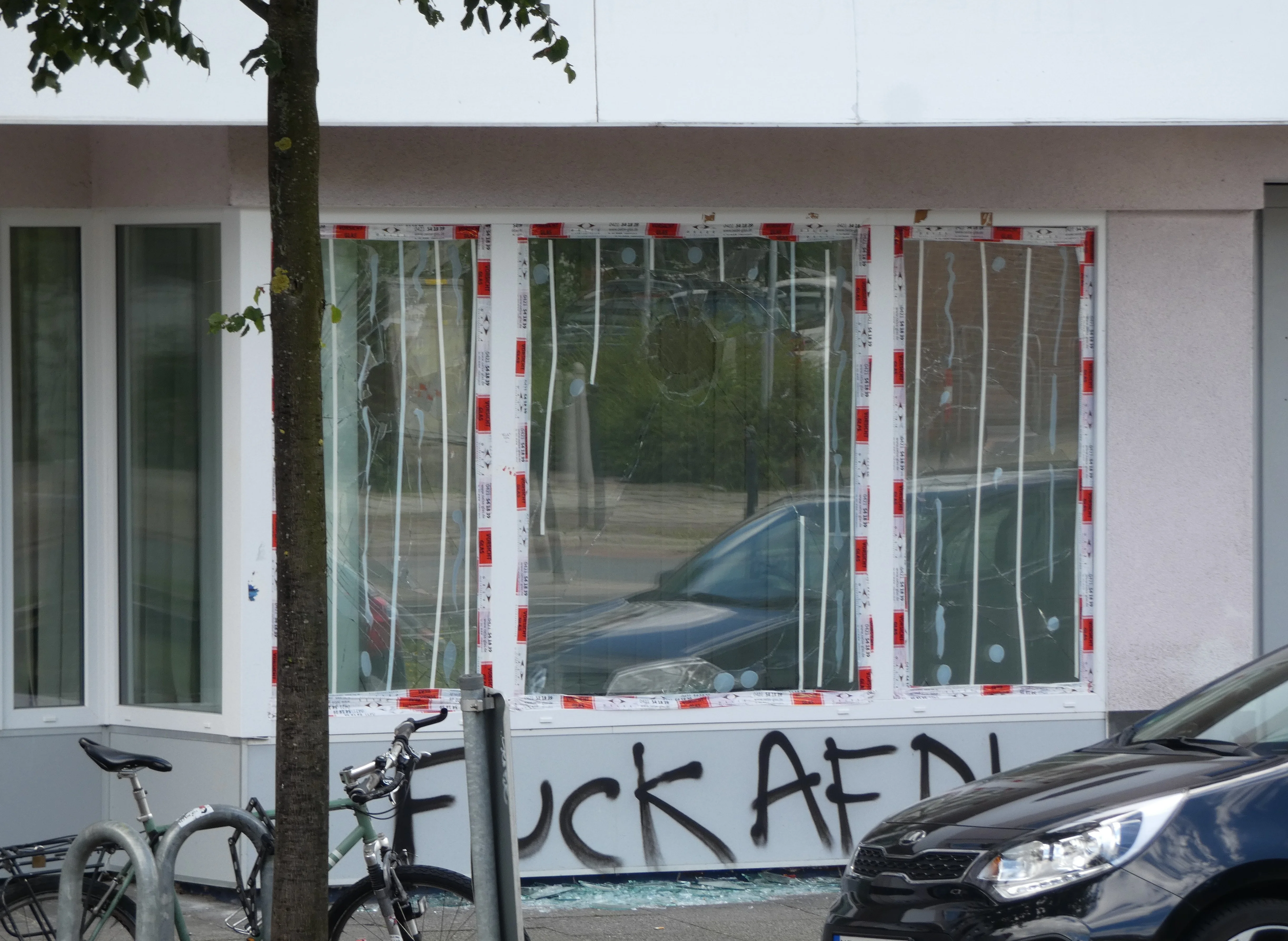 Beschädigte Scheiben der AfD-Geschäftsstelle. Glassplitter liegen auf dem Gehweg; unter den Fenstern steht „Fuck AFD!“.