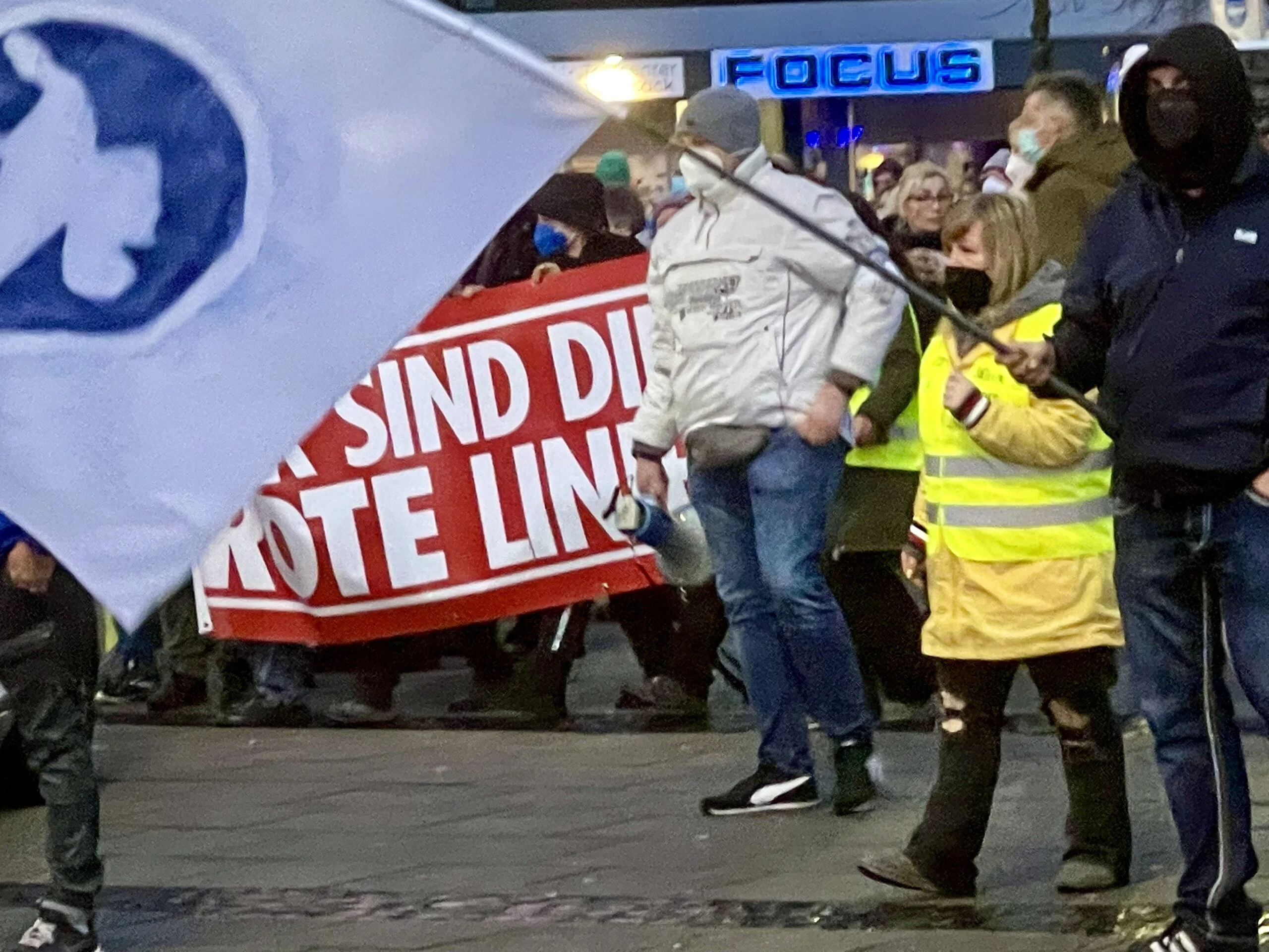 Abendlicher Demonstrationszug in Vegesack mit Ordner:innen in Warnwesten und einem roten Transparent.
