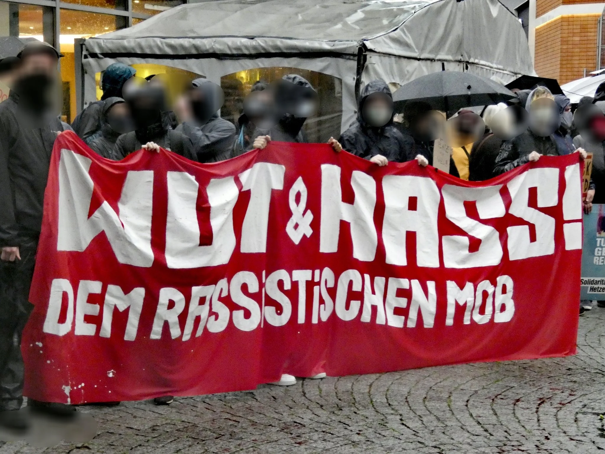 Demonstrierende halten ein rotes Transparent mit der Aufschrift „Wut & Hass! Dem rassistischen Mob“.