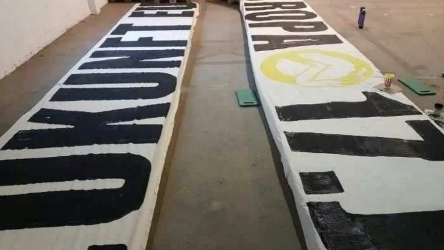 Große bemalte Transparente mit IB-Symbolik auf dem Boden einer Halle; nach der ursprünglichen Recherche in der Spedition Drewes.