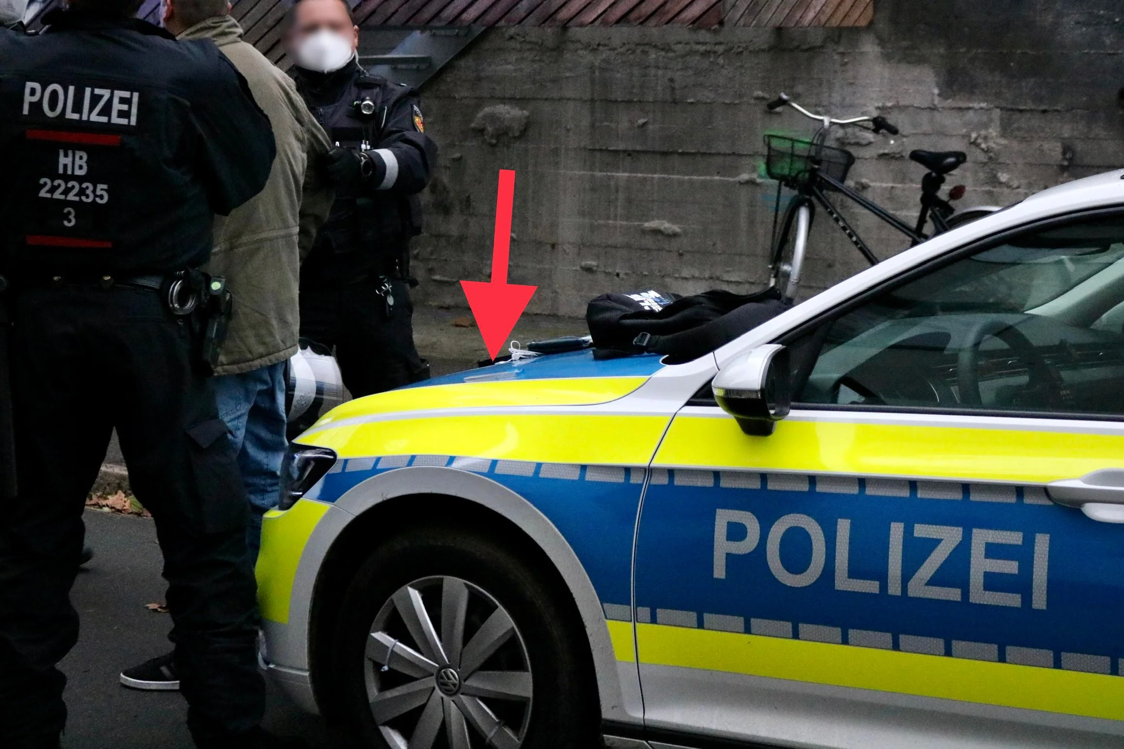 Polizeiliche Kontrolle neben einem Streifenwagen; ein bereits im Original eingefügter roter Pfeil weist auf einen Gegenstand auf der Motorhaube.